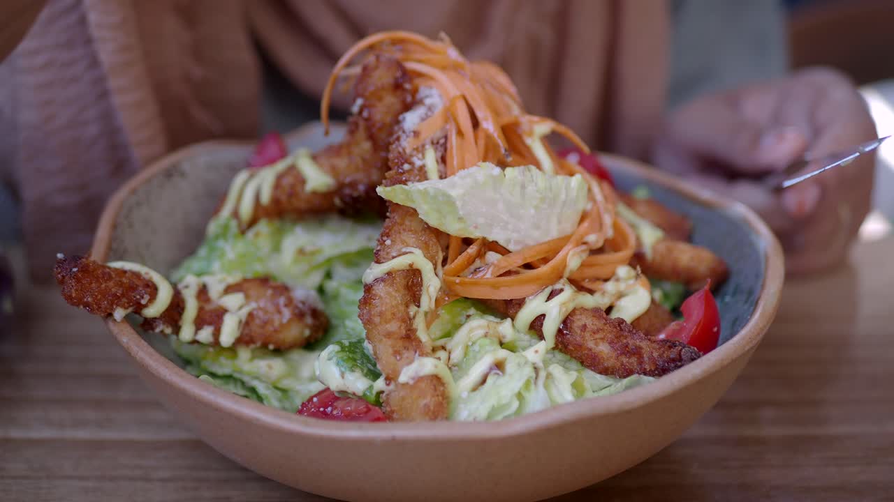 Woman eating a Caesar salad with crispy fried chicken