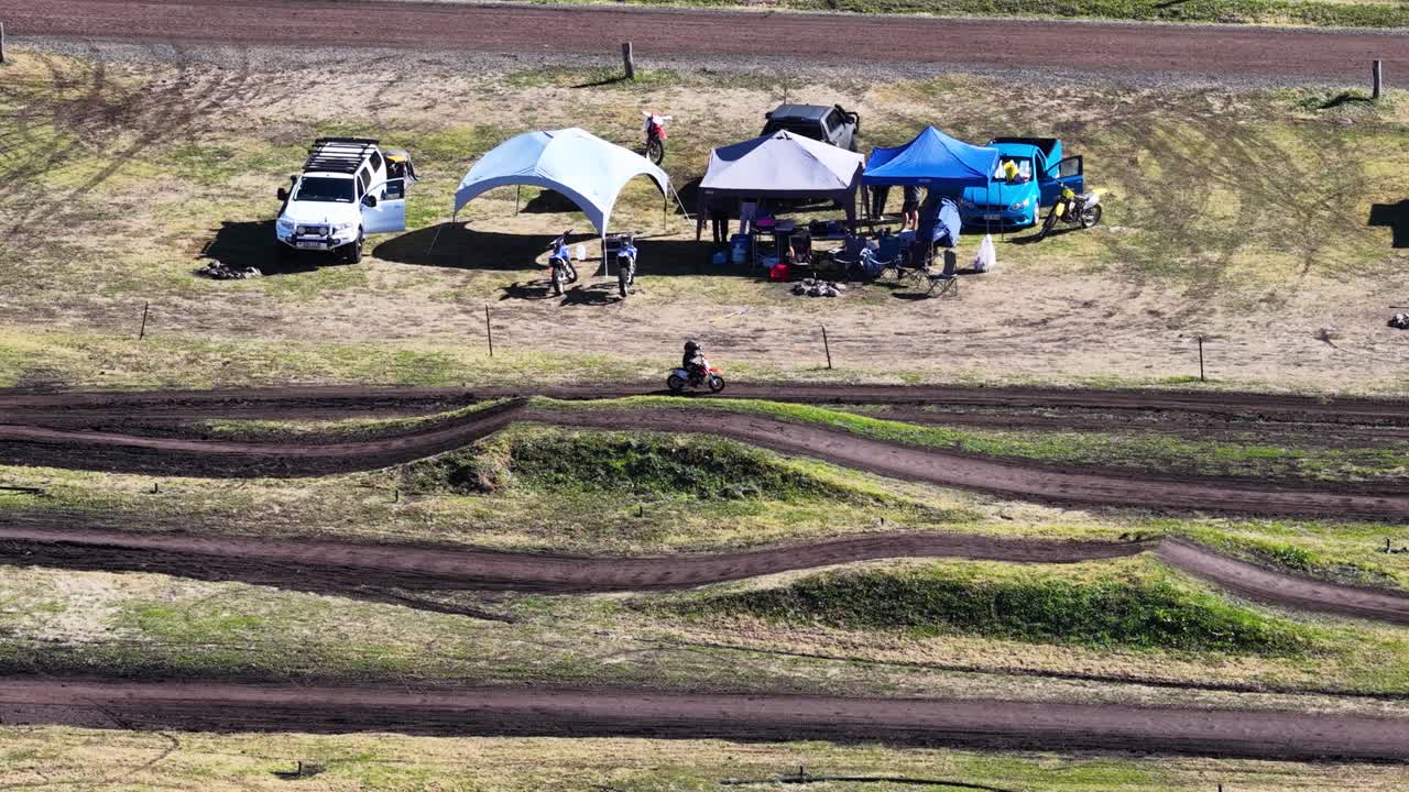 Young rider navigates winding dirt track under bright sunlight at rural motocross park