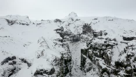 aerial close up approaching deep frozen snow covered canyon with high rocky cliffs in iceland.