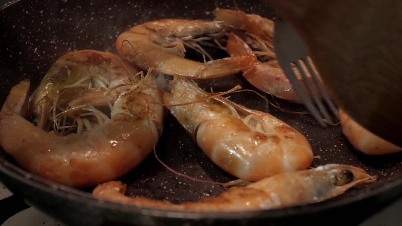 Cottura di gamberi reali in padella con una spatola di legno, sfrigolanti e saporiti.