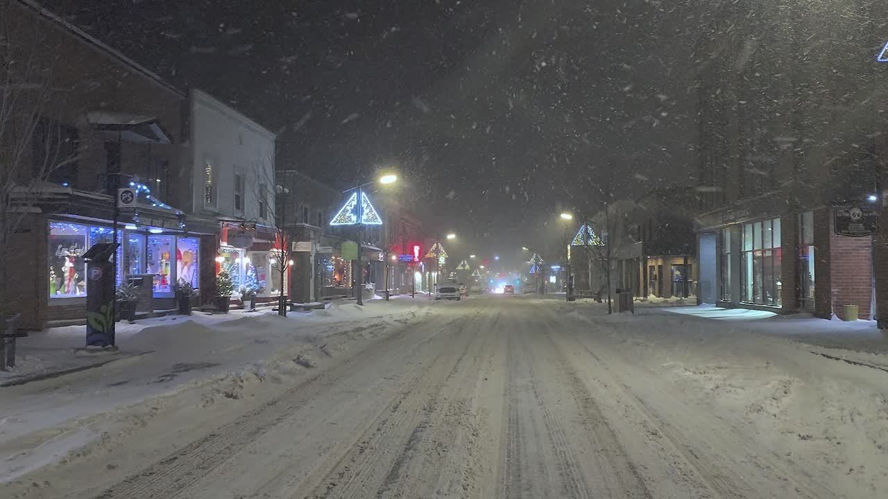 Close-up of a snow-covered Quebec street with shops on both sides as it snows