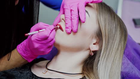 cosmetic procedure on lips in a beauty salon. master in pink latex gloves draws the client's lips with a red pencil. permanent makeup on lips.