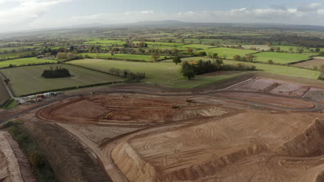 Revealing-drone-shot-of-a-sand-quarry,-with-diggers-and-bulldozer,-surrounded-by-the-British-countryside