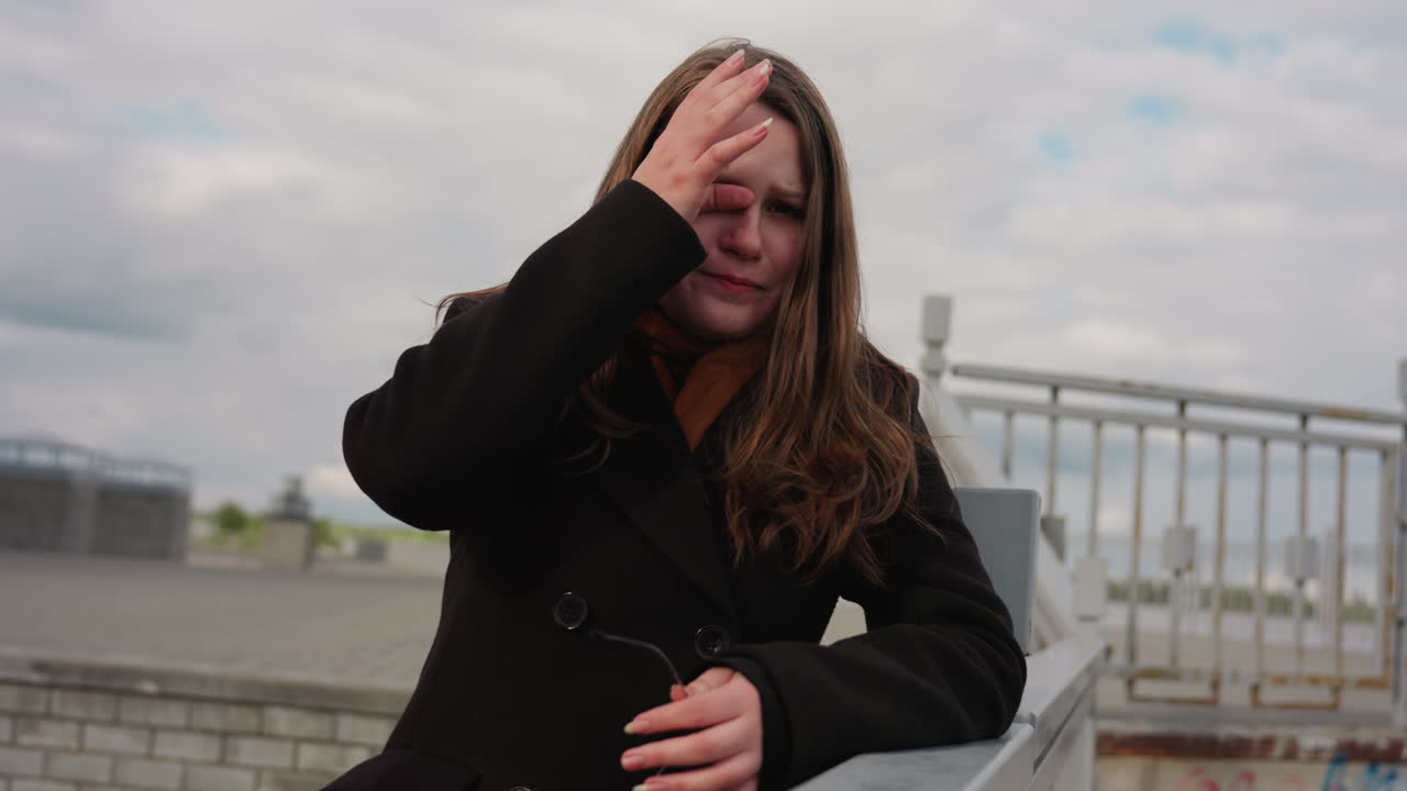 Urban sightseer pauses in quiet reflection, emotion filling face as tear drops under dusty sky, sunlight touching glasses and coat, expressing nostalgia and deep thought in peaceful city setting