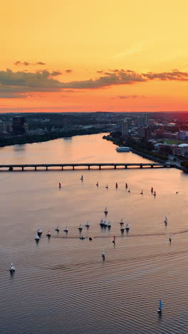 Approaching the group of yachts sailing by the Charles River in Boston, USA. Drone flying above the water. Beautiful orange sky at backdrop.. Vertical video