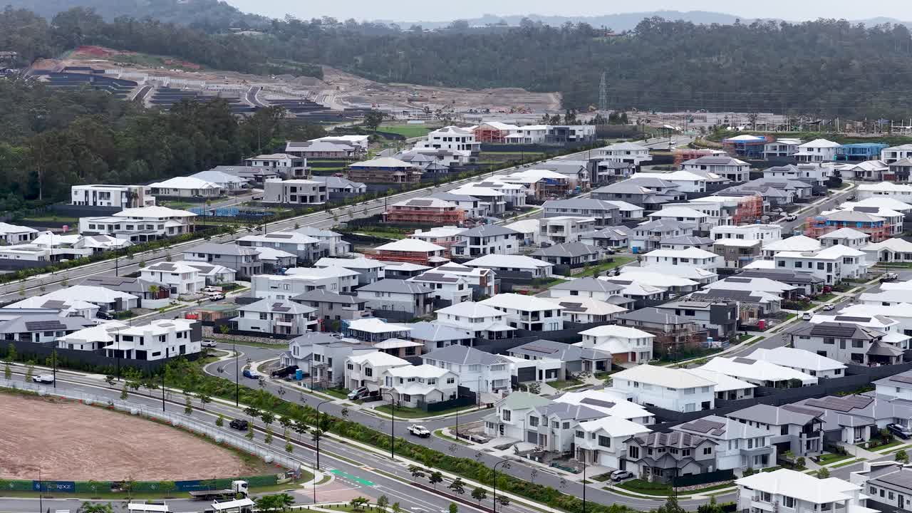 Drone pans above contemporary suburban homes, mountain backdrop, overcast daylight, wide landscape view