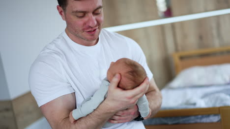 broad-shouldered man wearing white t-shirt waving his newborn child. dad taking care of the child while mom is resting.