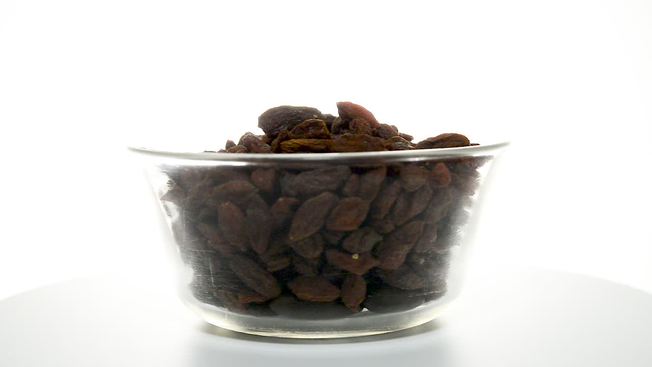 Dried goji berries in a glass bowl rotating on a white background