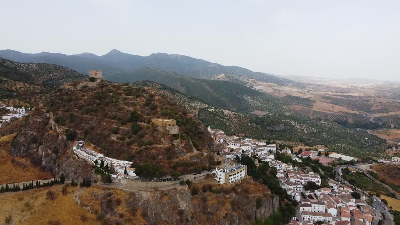 Ripresa aerea di un castello medievale in cima a una collina e di un borgo con case bianche tradizionali.