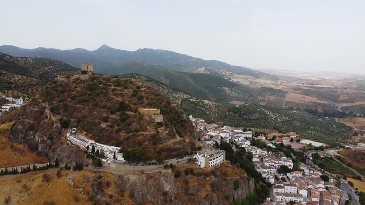 Ripresa aerea di un castello medievale in cima a una collina e di un borgo con case bianche tradizionali.