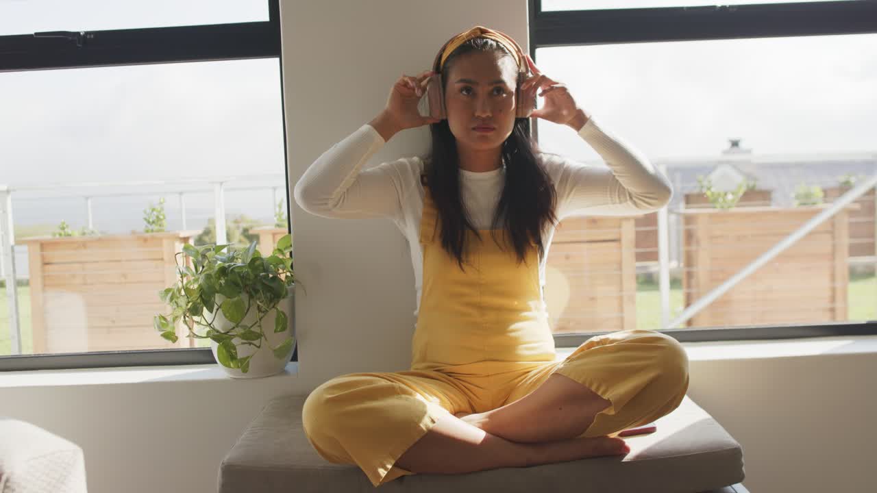 Donna asiatica che indossa le cuffie, se le sistema sulle orecchie, chiude gli occhi e ascolta musica a casa