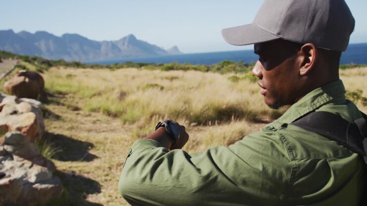 African american man hiking in countryside by the coast using smartwatch