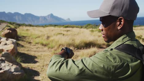 hombre afroamericano caminando por el campo junto a la costa usando un reloj inteligente