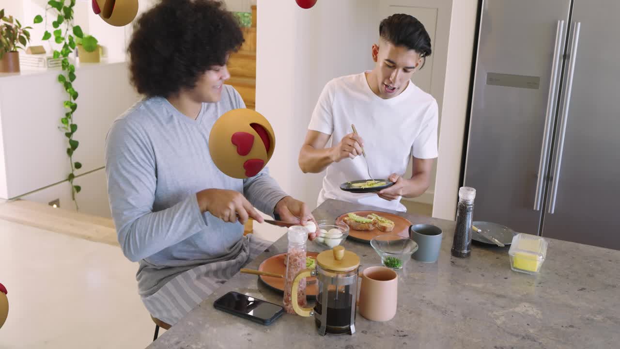 Dos hombres preparando el desayuno en una isla, pasándose un aguacate mientras aparecen y se desplazan superposiciones de emoji