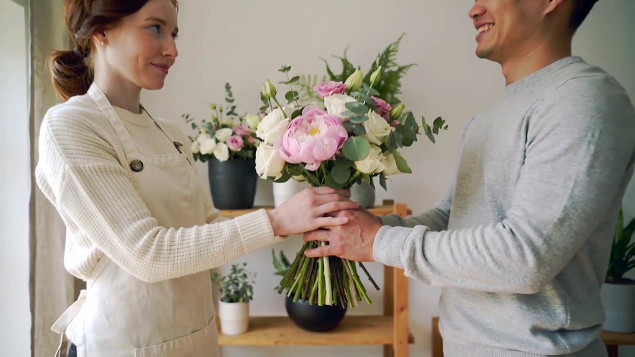 Un fiorista con grembiule e un cliente in maglione si scambiano un bouquet legato con spago in negozio per il ritiro.