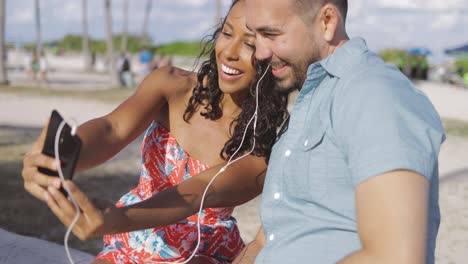 Laughing-couple-sharing-smartphone-and-headphones