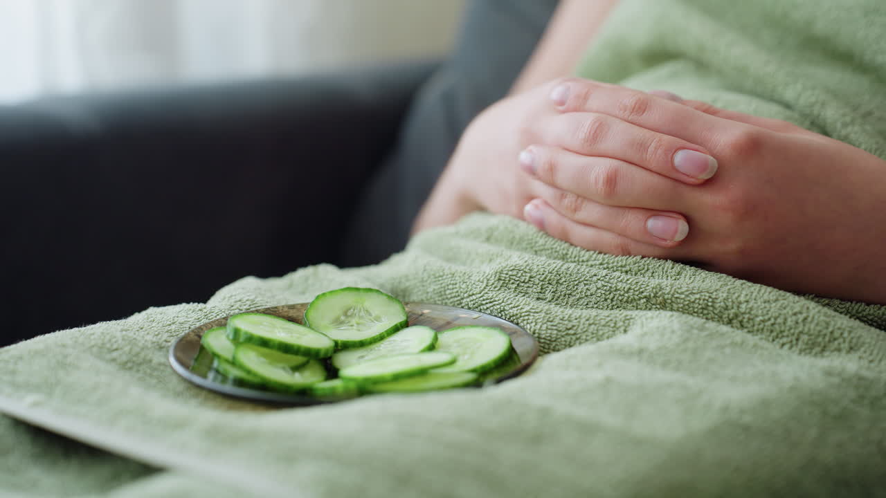 Close-up view of plate with cucumber slices placed on towel with hand gently resting nearby, peaceful spa experience, skincare treatment, and wellness concept