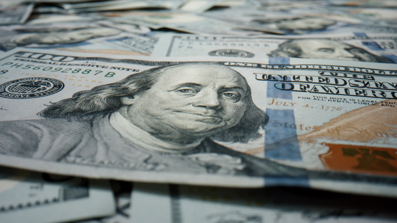 un billete de cien dólares de primer plano en un gran montón de moneda estadounidense en rotación.