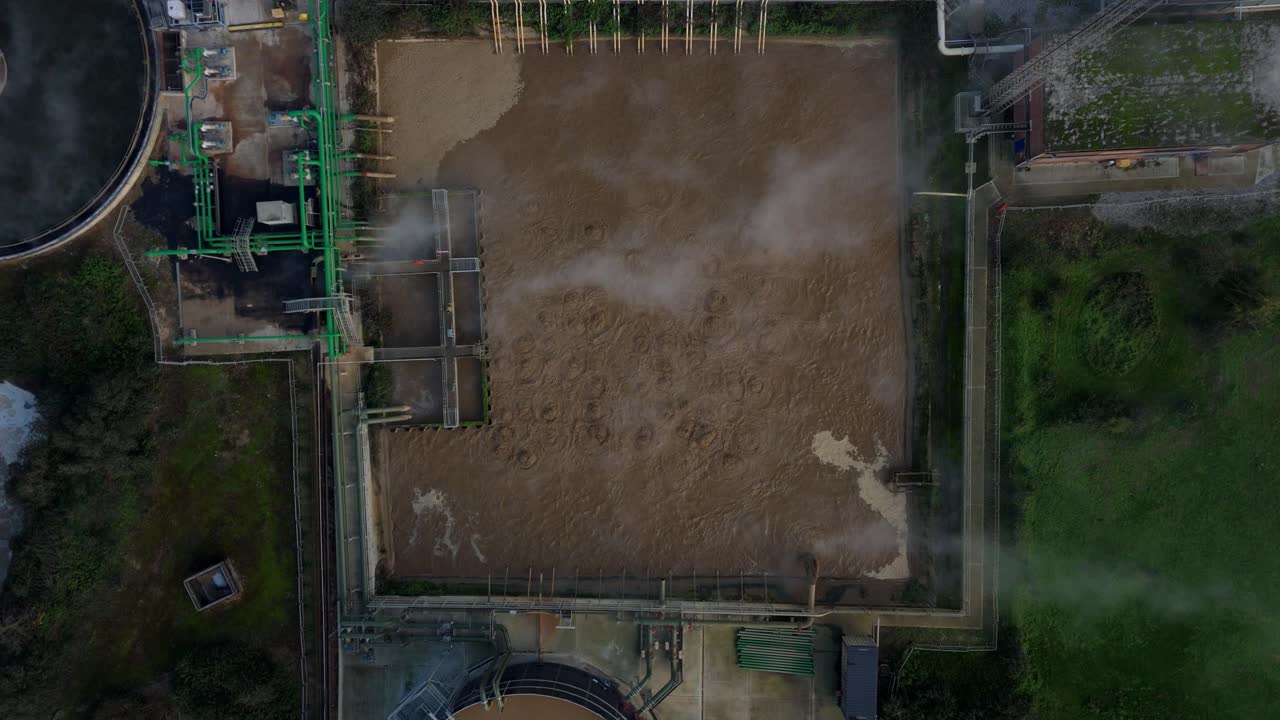 Volo di drone sopra le vasche di chiarificazione e le lagune di raffreddamento di uno zuccherificio, che mostrano sedimenti e liquido marrone in grandi bacini industriali nel Regno Unito.