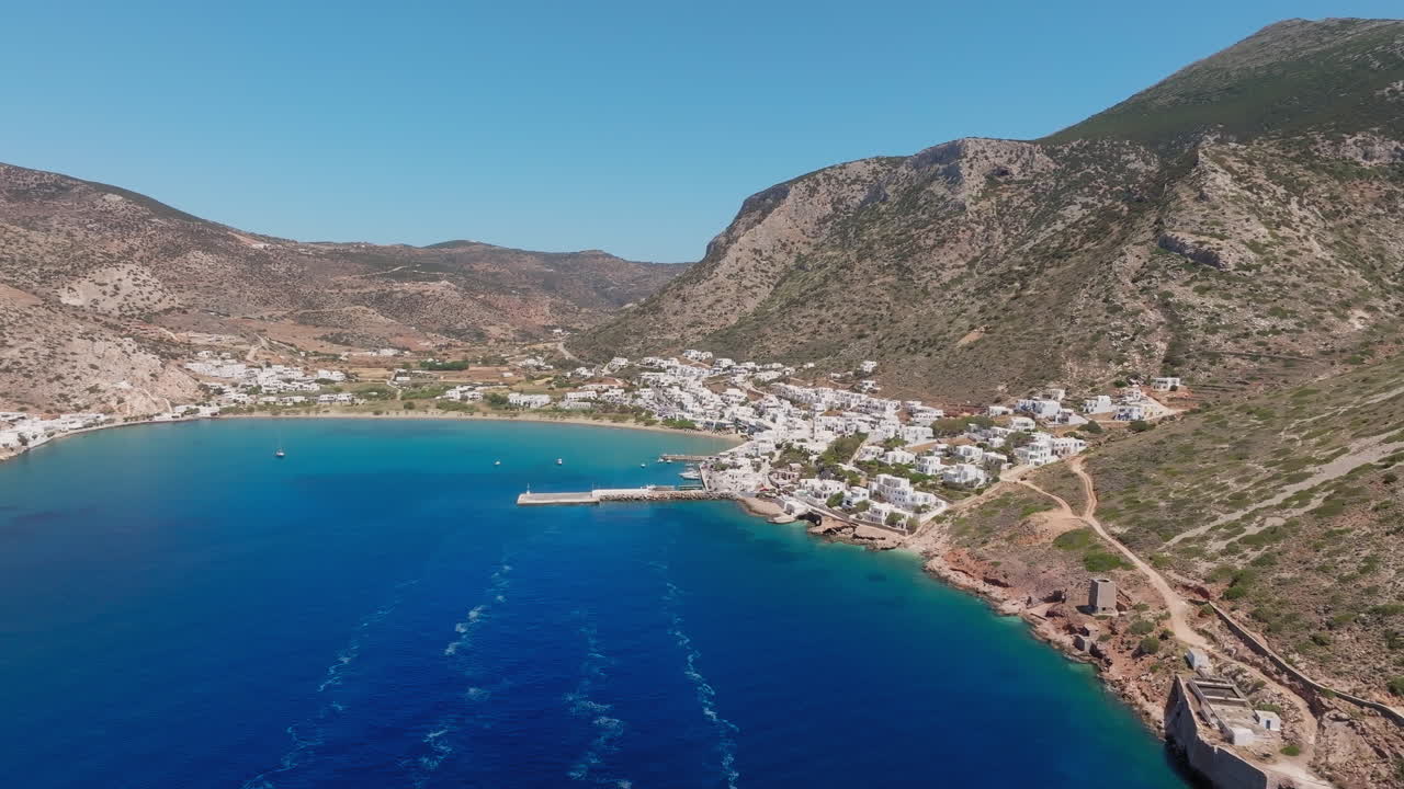 Drone pullout from Sifnos port over Kamares Bay showing water, boats, and Cycladic landscape