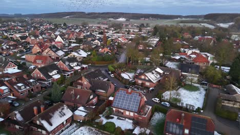 Houses and homes during snowy winter day in Germany. Neighborhood with snowy grass in garden. Aerial flyover of small town. Solar panels production on roof. Wide shot.