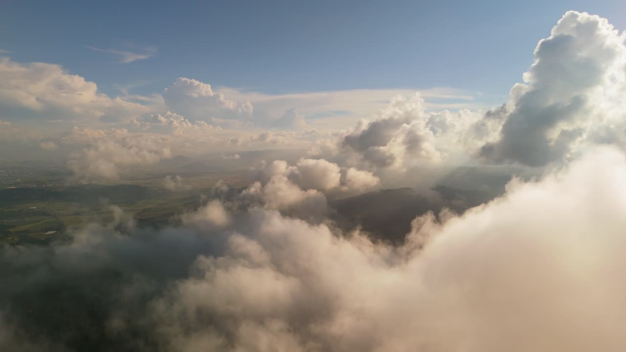 Fluffy clouds drift over rolling green fields under warm sunlight in a scenic aerial view
