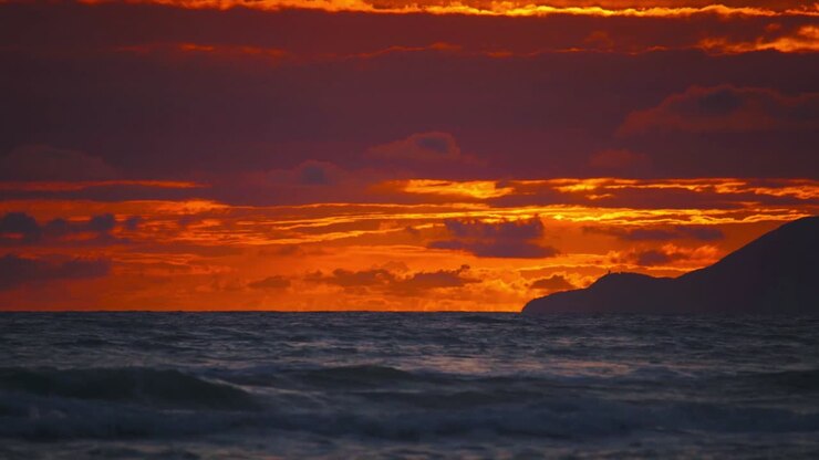 Cinemagraph / seamless video loop of a vibrant red sunset at a remote natural Tuscany seaside sand beach in Italy with dramatic sky and panoramic sea view. Blue and turquoise water at the scenic nature tourist vacation location.