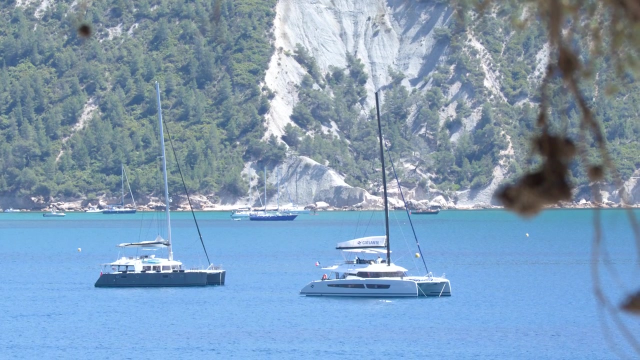 Inquadratura ampia statica di catamarani di lusso ancorati in acqua turchese contro aspre scogliere calcaree