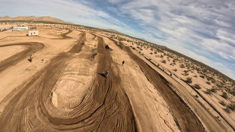 following a motorcycle as the rider speeds down a dirt track and jumps obstacles - first-person view drone