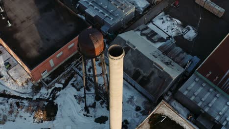 drone shot flying over a rusted water tower and smokestack in an abandoned industrial area in a small canadian town of thurso quebec