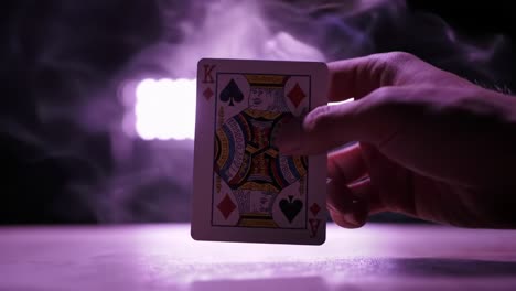 a hand holding a playing card illuminated by vibrant lights: a captivating display of cardistry and atmospheric effects in an enigmatic setting