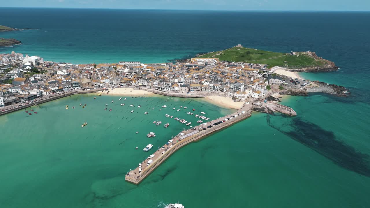 High aerial orbit of St Ives with boat exiting the bay into calm turquoise sea
