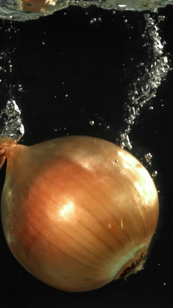 Cipolla fresca che si immerge nell'acqua con bolle al rallentatore.