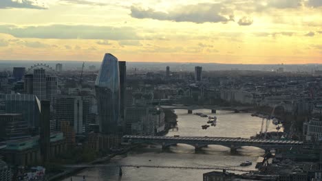 aerial wide shot of river thames during dusk with london eye and london bridge during sunset