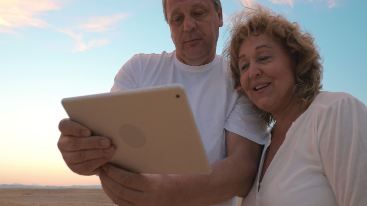 hombre y mujer mayores con computadora tablet en la playa