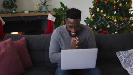 Lächelnder-Afroamerikanischer-Mann,-Der-Einen-Videoanruf-Führt,-Küsse-Sendet,-Weihnachtsdekorationen-Im-Hintergrund