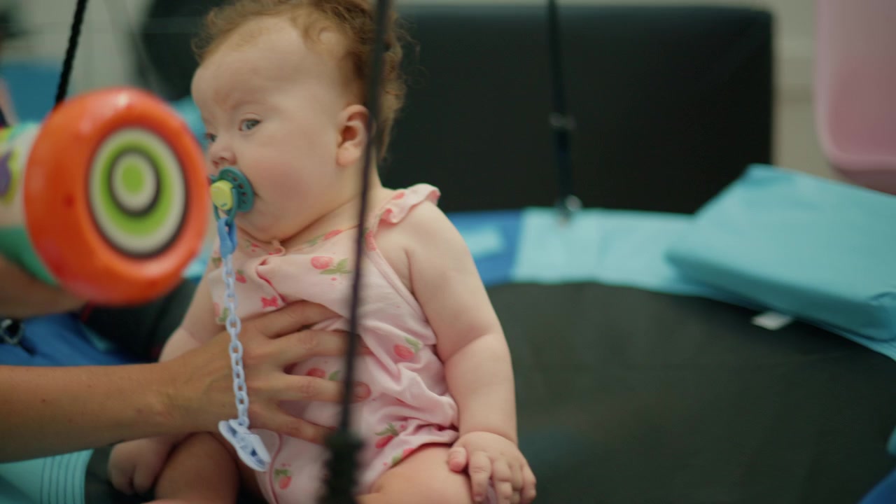 Baby girl with a pacifier held by an adult during a developmental therapy session, focusing on early intervention and support