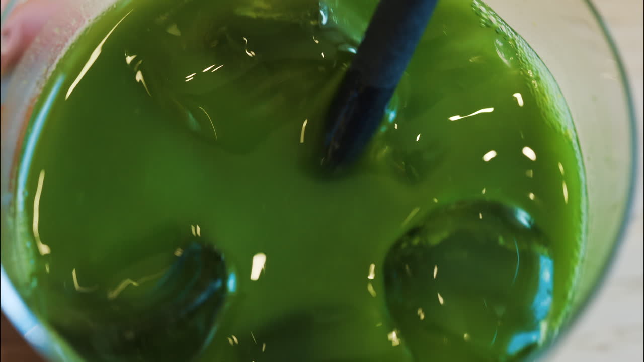 Close up of a hand mixing an iced matcha in a glass with a black straw at a cafe