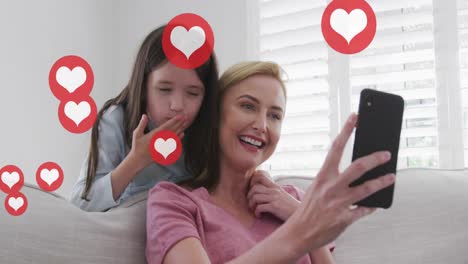 Animation-of-heart-icons-over-caucasian-blonde-mother-and-daughter-talking-on-smartphone-at-home