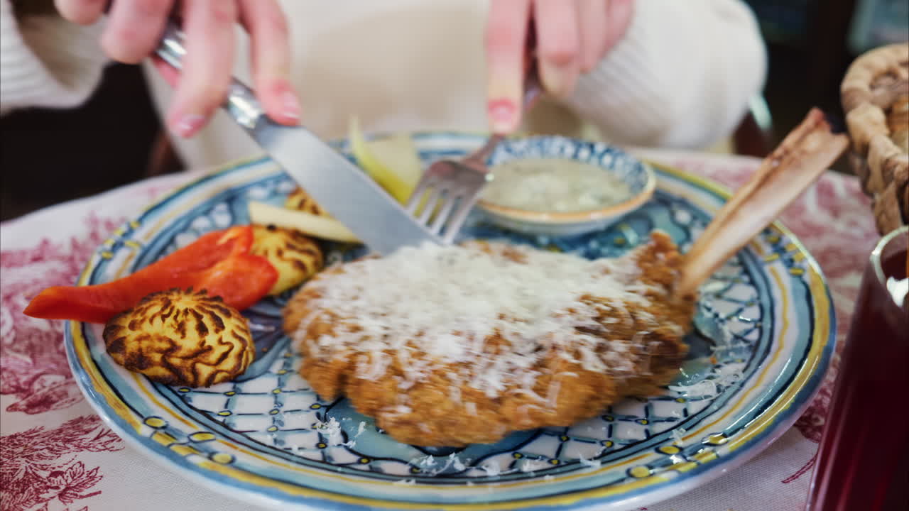 Close up of a woman cutting a piece of paneed meat and dipping it in sauce at a restaurant