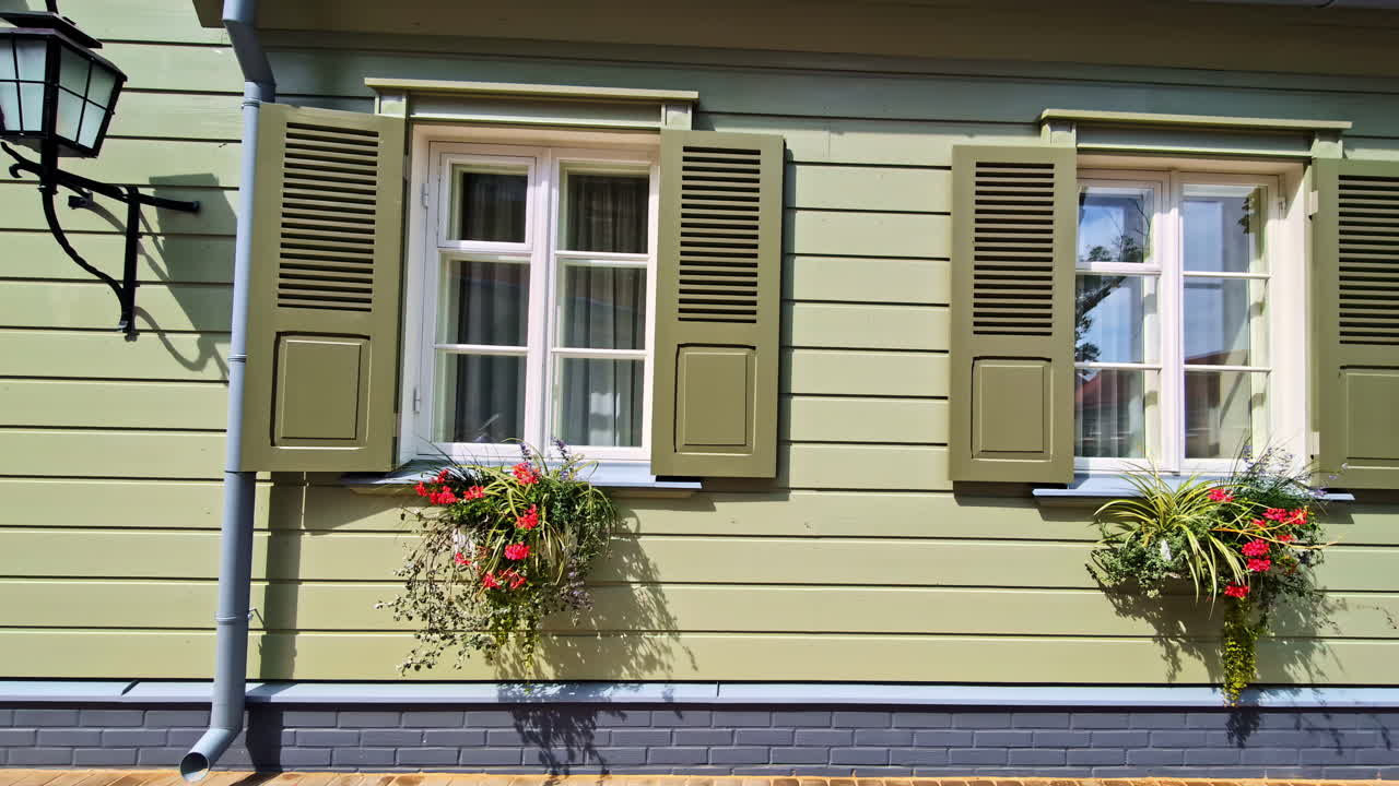 Green wooden house wall with flower boxes and open white window shutters