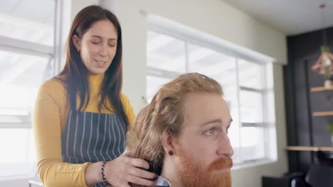 una peluquera caucásica desatando el cabello largo de un cliente masculino y aconsejando en el salón, en cámara lenta.