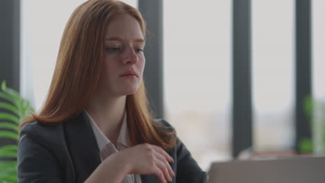 A-young-red-haired-business-woman-looks-thoughtfully-at-the-screen-and-brainstorms.-Watch-and-think-about-problems-looking-out-the-window.-Thoughtful-business-woman