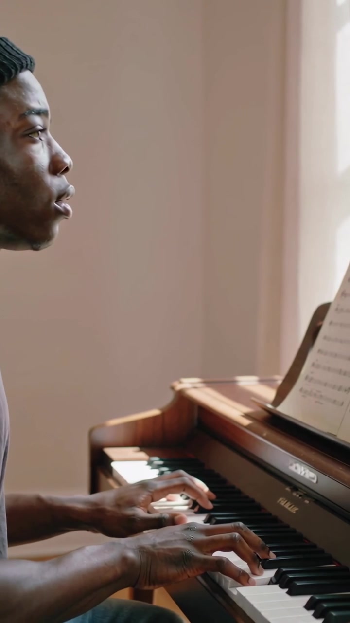 Vertical video: Reading sheet music urging man in black beanie playing piano at window, copy space
