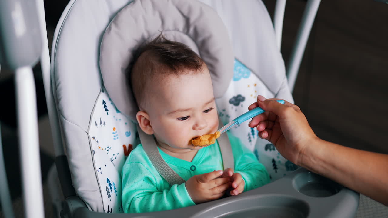 Mother is feeding her beautiful sweet child. Mom's hand shoves full spoon into baby's mouth. High angle view.
