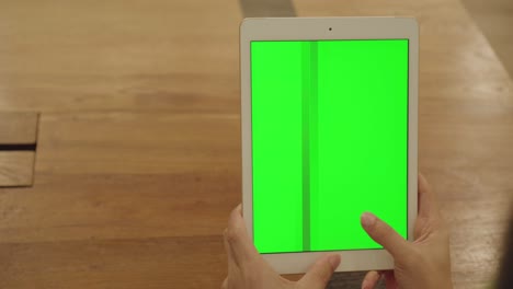 hombre con la mano sosteniendo una tableta con una pantalla verde en blanco y los dedos tocando y deslizando en la pantalla.