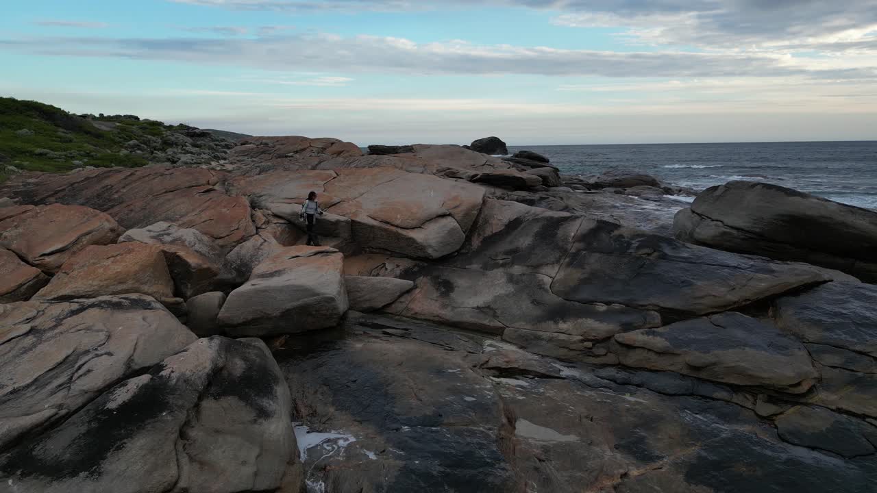 Donna che cammina sulle rocce di fronte all'oceano al tramonto, Red Gate Beach, Australia Occidentale