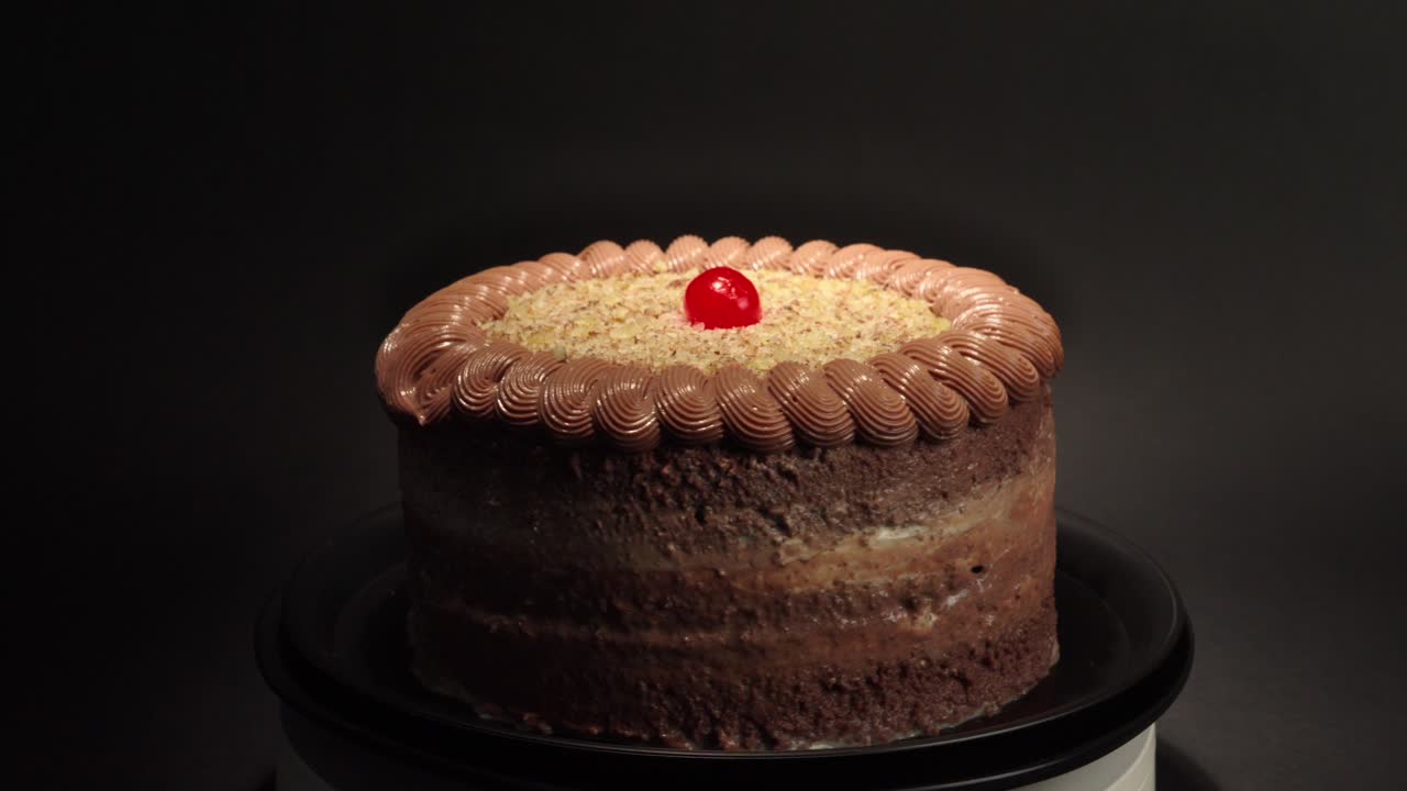 Sjokolade- og ostekake på et roterende fat med svart bakgrunn, med kirsebær på toppen og nøtter, velsmakende og fristende.