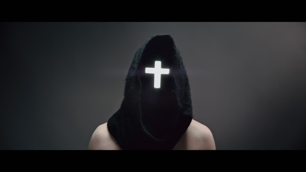 Masked and hooded man with cross of light glowing on his face rise his head