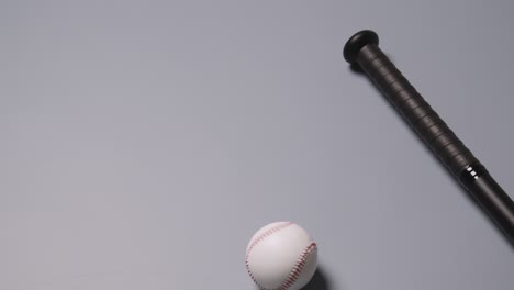 vida muerta de béisbol con murciélago y pelota rodando en el marco contra un fondo gris